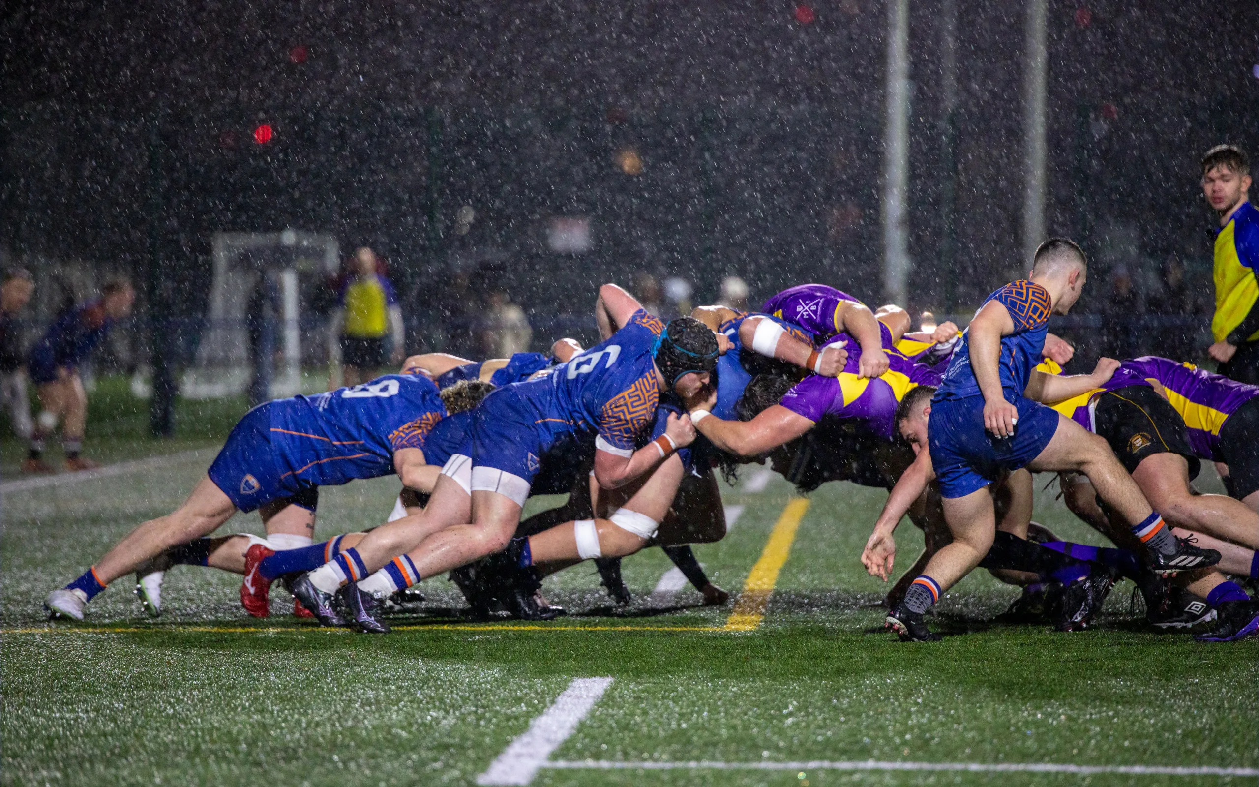 Mêlée de rugby de nuit sous la pluie et les projecteurs